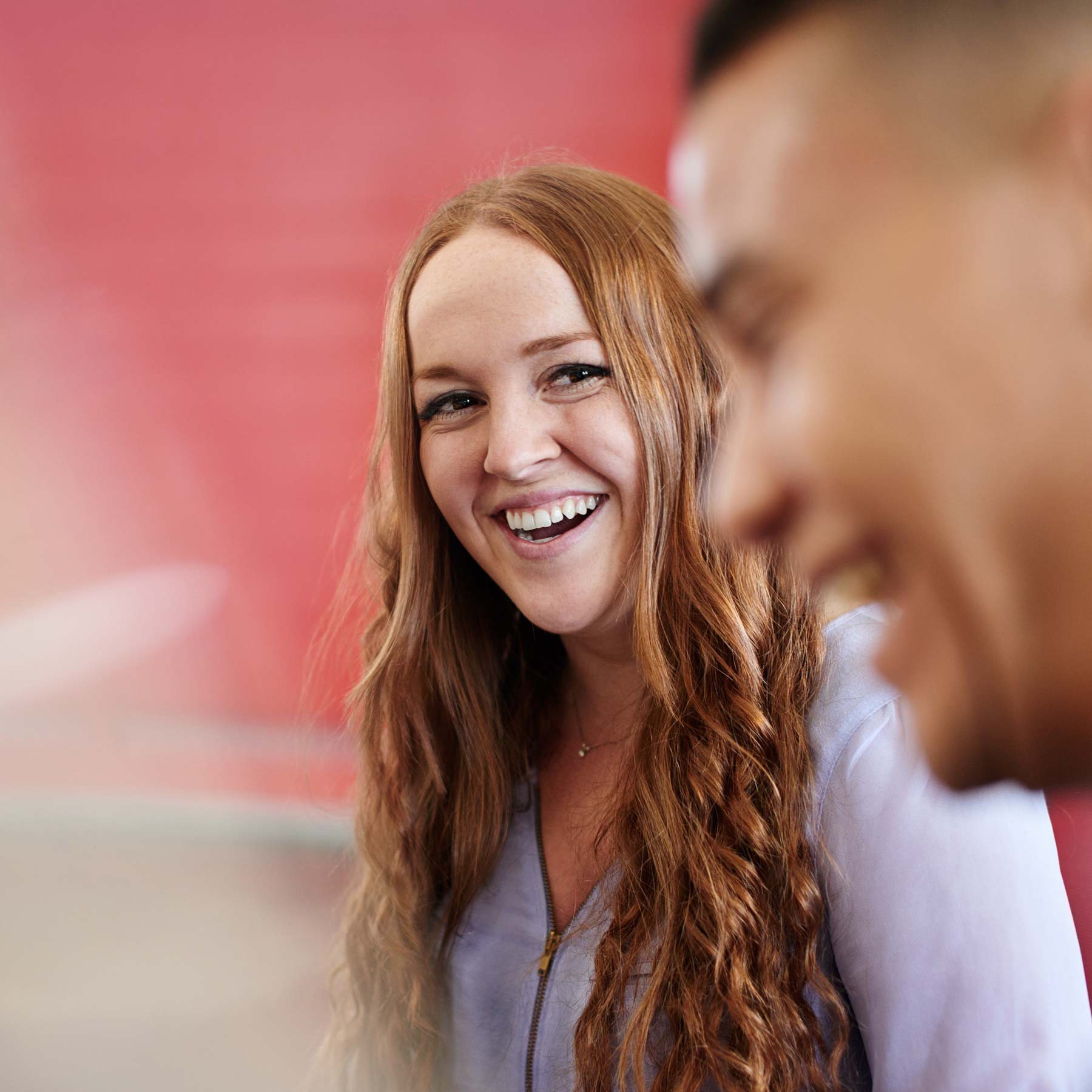 A long-haired redhead woman smiling at a laughing man in the foreground